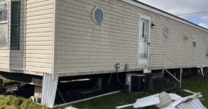 Mobile home with damaged skirting panels removed, exposing foundation supports and underside structure