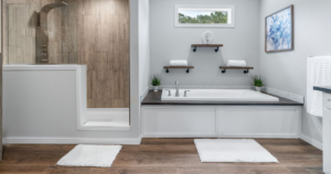 Modern mobile home bathroom remodel featuring waterproof wood-look flooring, a walk-in shower with tile walls, and a soaking tub in a bright, contemporary space.