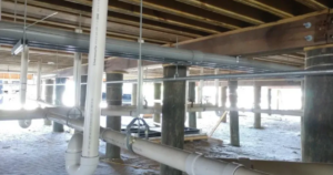 PVC plumbing pipes and drainage system installed beneath a raised mobile home supported by pilings.